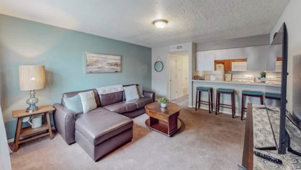 A modern living room with a sectional sofa, a coffee table, and a TV. A kitchen area with bar stools is visible in the background. - Mountain Road Hideaway, near Old Town (Albuquerque)