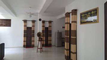 Un salón amplio con ventilador de techo, televisor y refrigerador.