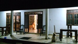 A covered outdoor area with a stone wall, wooden furniture, and a cat. - sinhagiri hotel and restaurant (Tangalle)