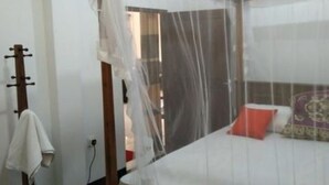 A bedroom with a four-poster bed, a wooden floor, a white wall, and a door with a towel hanging on it. - sinhagiri hotel and restaurant (Tangalle)
