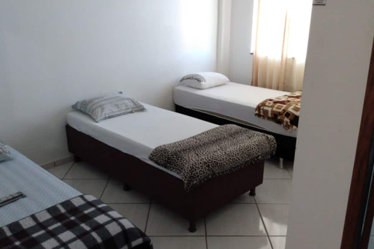 Una habitación pequeña y limpia con dos camas individuales, una con un edredón estampado de leopardo y la otra con una sábana blanca lisa.