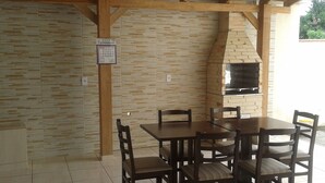 An outdoor patio with a brick wall, a wooden table and chairs, and a brick oven. - Hotel KM 73 (Araquari)