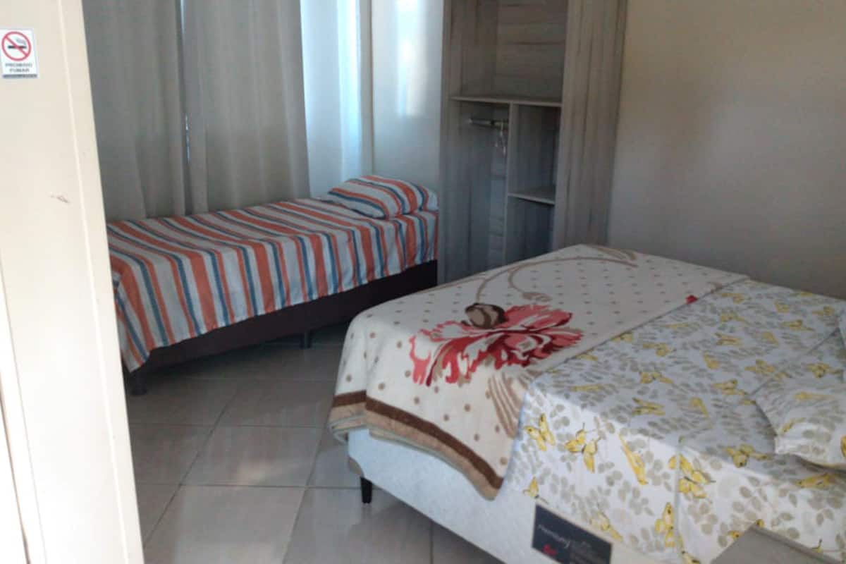 Un dormitorio con dos camas, una con ropa de cama a rayas y la otra con estampado floral. Hay un armario con espejo y una puerta.