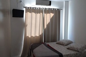 A room with a bed, a flat-screen TV mounted on the wall, and a window with curtains.