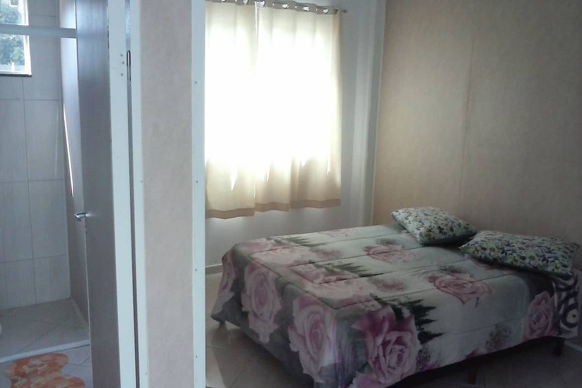 Un dormitorio con cama, ventana con cortinas y zona de ducha.