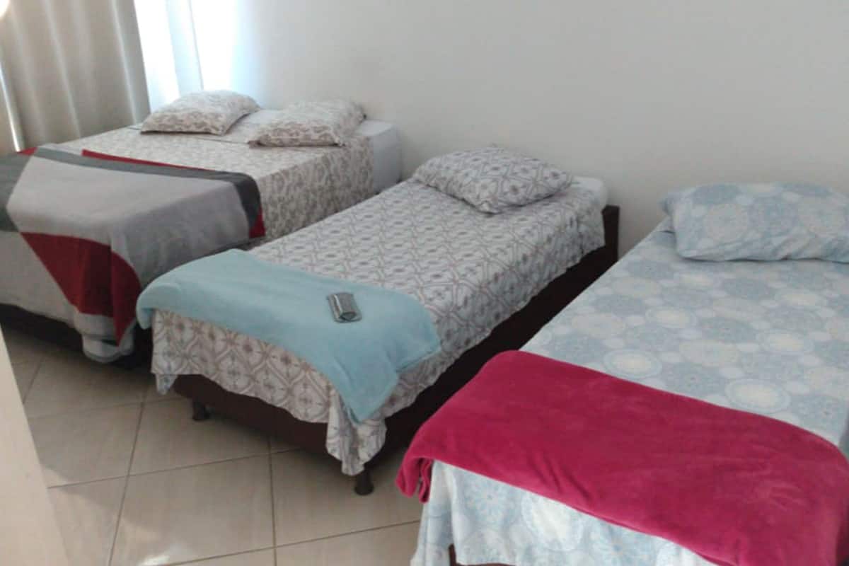 Habitación de hotel con tres camas individuales, cada una con una colcha y almohadas estampadas.