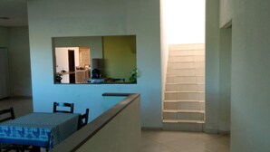 A dining area with a table and chairs, a kitchen area with a counter and appliances, and a staircase leading to an upper level. - Hotel KM 73 (Araquari)