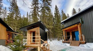 Two cabins with wooden exteriors, a deck, and a snowy forest background.