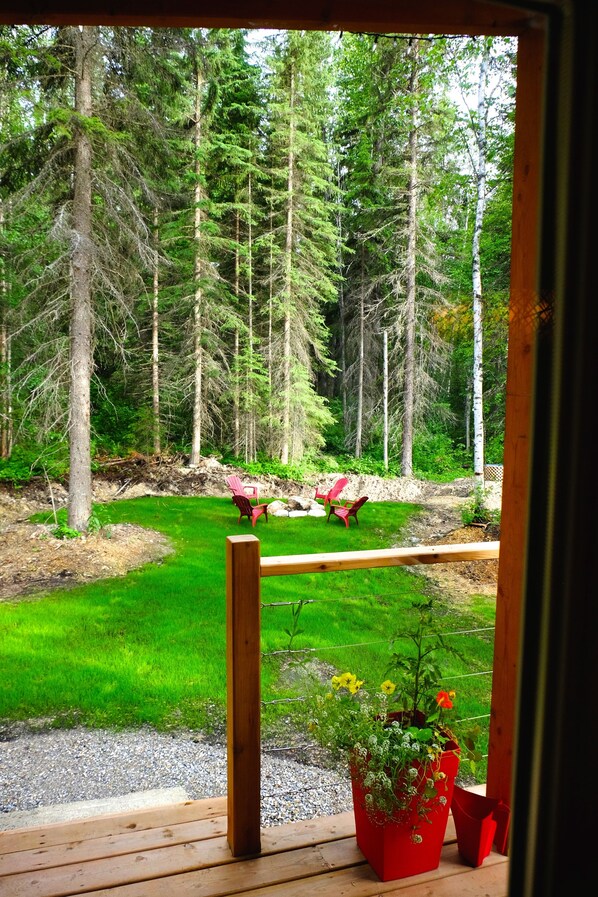 A wooden deck with a view of a forested area, two red chairs, and a potted plant with flowers.