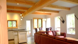 A spacious living area with a red sofa, wooden beams, and a view of the outdoors through large windows. - The Stag Chalet,  new Sauna in the forest! Fast wifi! (Golden)