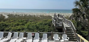 A beach view with a wooden staircase leading to a deck with white chairs. - 7 BR, 7.5 Baths Oceanfront with Pool and Hot Tub! Book your week of Permanent Waves!! (Brunswick)
