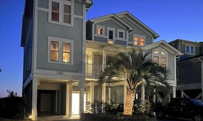 A multi-story residential building with a covered front porch, a palm tree, and a parked car. - 7 BR, 7.5 Baths Oceanfront with Pool and Hot Tub! Book your week of Permanent Waves!! (Brunswick)