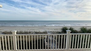 Uitzicht op een strand vanaf een balkon met een balustrade, de oceaan en een verre kustlijn.