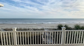 A beach view from a balcony with a railing, ocean, and a distant shoreline.