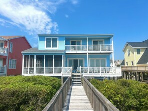 A two-story house with a balcony, a porch, and a wooden deck leading to the entrance. - 5 bedrooms, 5 bathrooms. Oceanfront with oceanside screened in porch and pet friendly. (Brunswick)