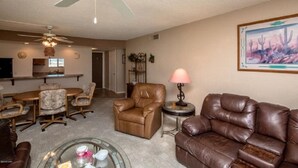 A living room with leather furniture, a glass coffee table, a ceiling fan, and a painting on the wall.