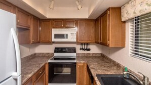 A compact kitchen with wooden cabinets, a white refrigerator, a microwave, an oven, and a sink.