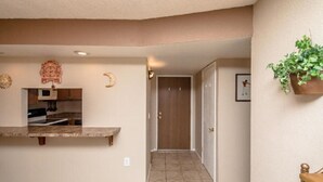 A hallway with a kitchen area, a door, and a plant on the wall.