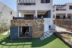 Ein modernes, zweistöckiges Haus mit Natursteinfassade, einem Balkon und einem kleinen Garten.