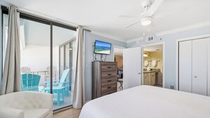 Ein Schlafzimmer mit einem Bett, einer Kommode, einem Fernseher und einer Glasfenstertür, die auf einen Balkon mit Stühlen führt.
