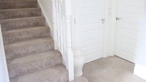 Een betegeld trappenhuis met witte balustrades, leidend naar een reeks witte deuren.