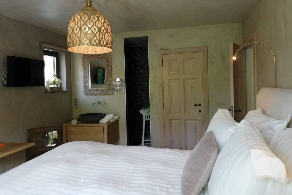 Une chambre à coucher avec un grand lit, une table de chevet, un miroir, un lavabo et un luminaire suspendu.