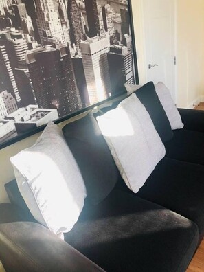 A black sofa with three white pillows against a wall with a cityscape poster. - Canal Waterfront Townhouse (Leeds)