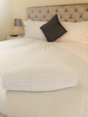 Un lit bien fait, avec du linge de lit blanc et un seul oreiller foncé.