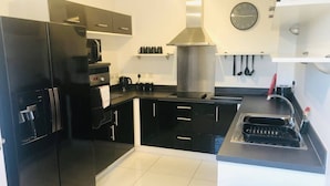 A modern kitchen with black cabinetry, a stainless steel range hood, a built-in microwave, and a sink with a faucet. - Canal Waterfront Townhouse (Leeds)