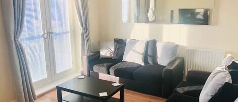 Ein Wohnzimmer mit einer Couch, einem Couchtisch und einem großen Fenster mit Vorhängen.