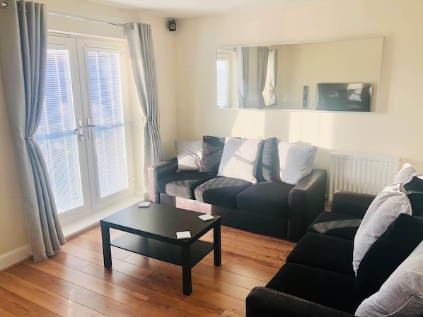 A living room with a sofa, a coffee table, and a large window with curtains.