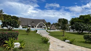 A resort with a pool, thatched-roof buildings, and a stone pathway leading to the pool area.