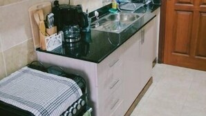 Cozinha compacta com armários brancos, bancada preta e cafeteira.