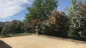 A fenced outdoor area with a dirt surface, surrounded by trees and a building in the background. - Holiday villa with pool in Vallon Pont d'Arc, near the Ardèche river (Vallon-Pont-d'Arc)