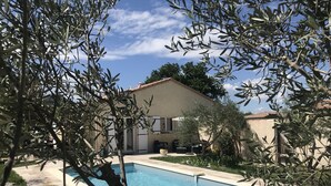 A swimming pool with a tiled deck, surrounded by olive trees and a building with a tiled roof. - Holiday villa with pool in Vallon Pont d'Arc, near the Ardèche river (Vallon-Pont-d'Arc)