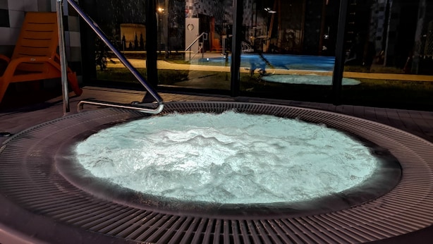 Un bain à remous doté d’une structure métallique et offrant une vue sur une piscine et un espace extérieur grâce à une paroi en verre.