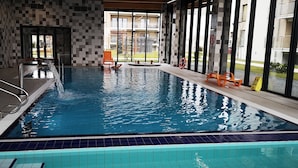 Une piscine intérieure à l’eau claire, avec des murs carrelés et une vue sur l’extérieur.
