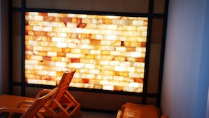 Une pièce dotée d’une grande fenêtre donnant sur un mur à la texture intéressante, des chaises en bois et un aménagement simple et moderne.