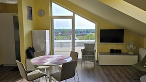 Une pièce moderne comprenant une table à manger, des chaises, un canapé, un téléviseur et donnant sur l’extérieur.