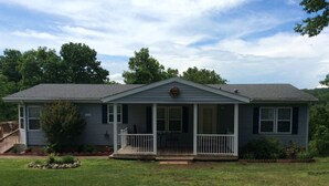 A single-story house with a front porch, a small deck, and a front yard. - Family Lake View Home - with Dock Access  (Sunrise Beach)