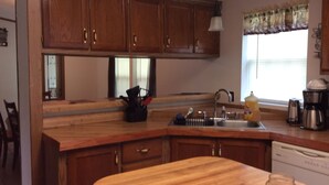 A kitchen with wooden cabinets, a sink, a coffee maker, and a window with a curtain. - Family Lake View Home - with Dock Access  (Sunrise Beach)