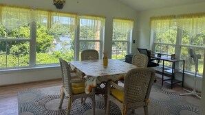 A dining area with a table and chairs, large windows with curtains, a ceiling fan, and a view of greenery and water outside. - Family Lake View Home - with Dock Access  (Sunrise Beach)