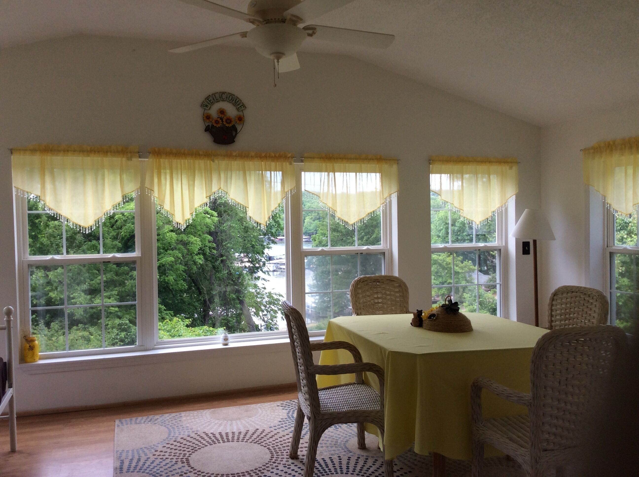 A dining area with a table and chairs, large windows with curtains, a ceiling fan, and a view of greenery outside.