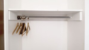 Un armario blanco con una barra para colgar perchas de madera y otra barra metálica.