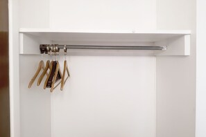 A white closet with a rod holding wooden hangers and a metal rod. - OYO Hotel Kings at Clovis (Clovis)