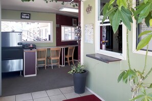 A compact kitchen with a refrigerator, a dining area with chairs, and a potted plant. - OYO Hotel Kings at Clovis (Clovis)