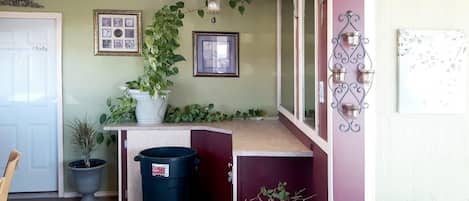 Una habitación con una puerta, un cubo de basura, una planta en maceta y una pared con cuadros.