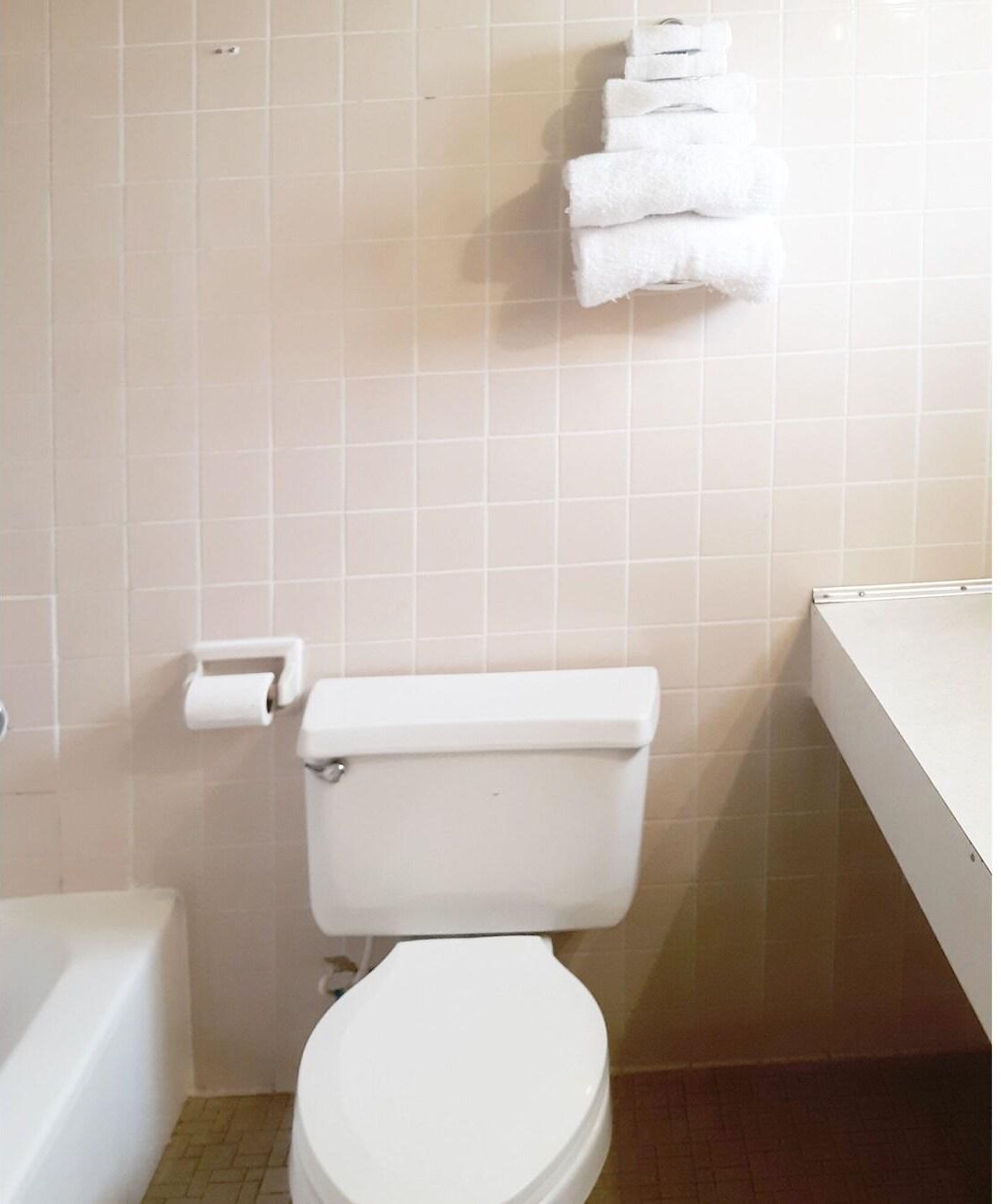 A bathroom with a toilet, a roll of toilet paper, and a stack of white towels on a wall.