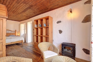 A cozy room with a wooden ceiling, a bed, a wicker chair, a bookshelf, and a wood-burning stove. - Living in a stylishly renovated town house in Santa Cruz de la Palma (santa cruz de la palma)