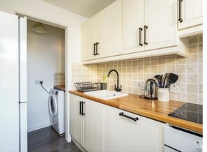 Une cuisine de taille réduite, dotée d’un plan de travail en bois, d’un évier encastré et de meubles de rangement blancs.